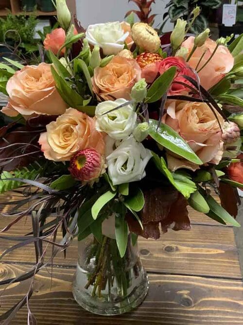 Flower arrangement with warm peach and creamy white blooms, mixed with rich greenery and deep burgundy foliage