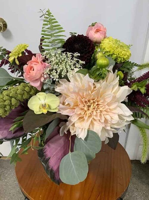 Flower arrangement with a blend of soft blush and deep purple, with green accents