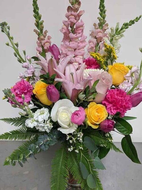 Flower arrangement that combines bright pinks, yellows, and soft whites, with fresh greenery mixed within