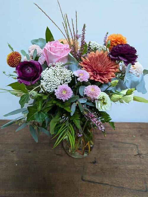 Flower arrangement containing rich hues and layered greenery