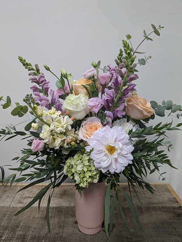 Flower arrangement with soft hues, including warm blush, delicate ivory, and airy greenery